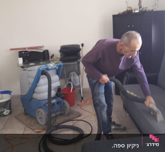 אדם מנקה ספה עם שואב אבק מקצועי